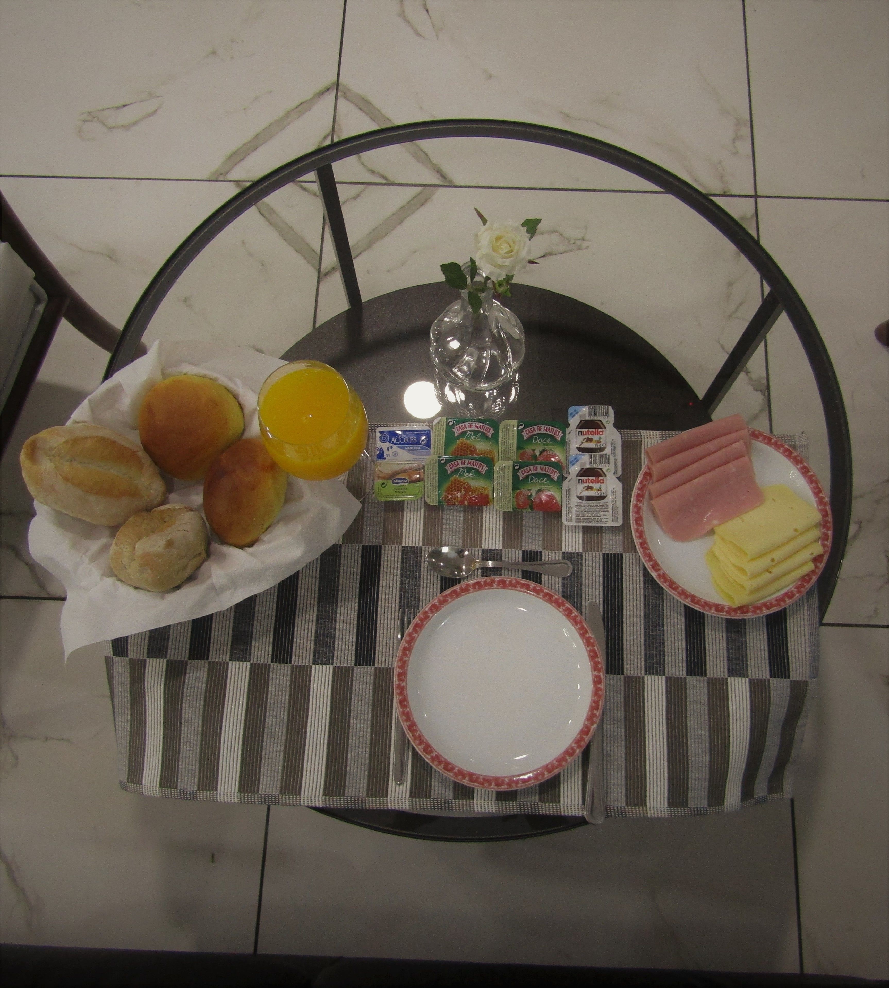 Una mesa con un mantel a rayas, con pan, jugo, Nutella y queso para el desayuno.