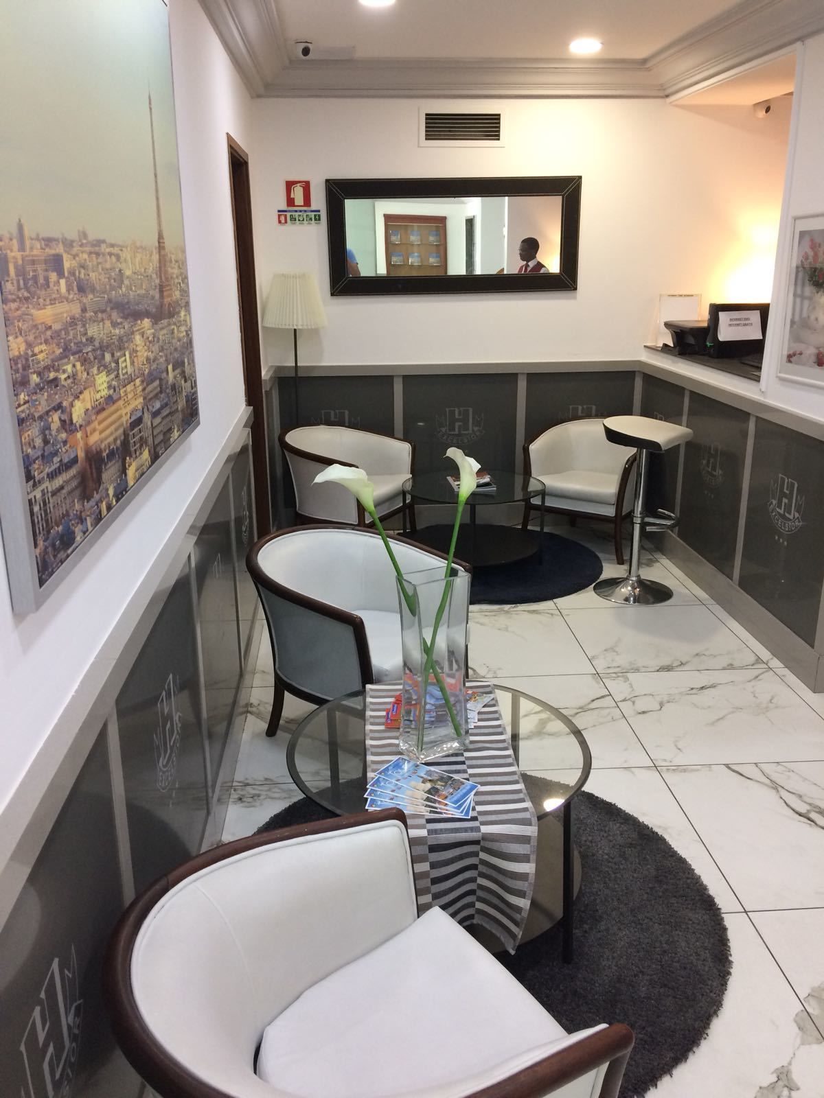 A hotel lobby with a reception desk, seating area, and a large cityscape painting on the wall.