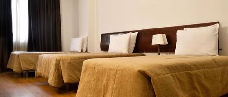 Ein Hotelzimmer mit drei Einzelbetten, jeweils mit brauner Bettdecke und weißen Kissen. Am rechten Rand des Zimmers ist ein Holzkopfschild zu sehen, und ein Nachtlicht steht auf dem Nachttisch.