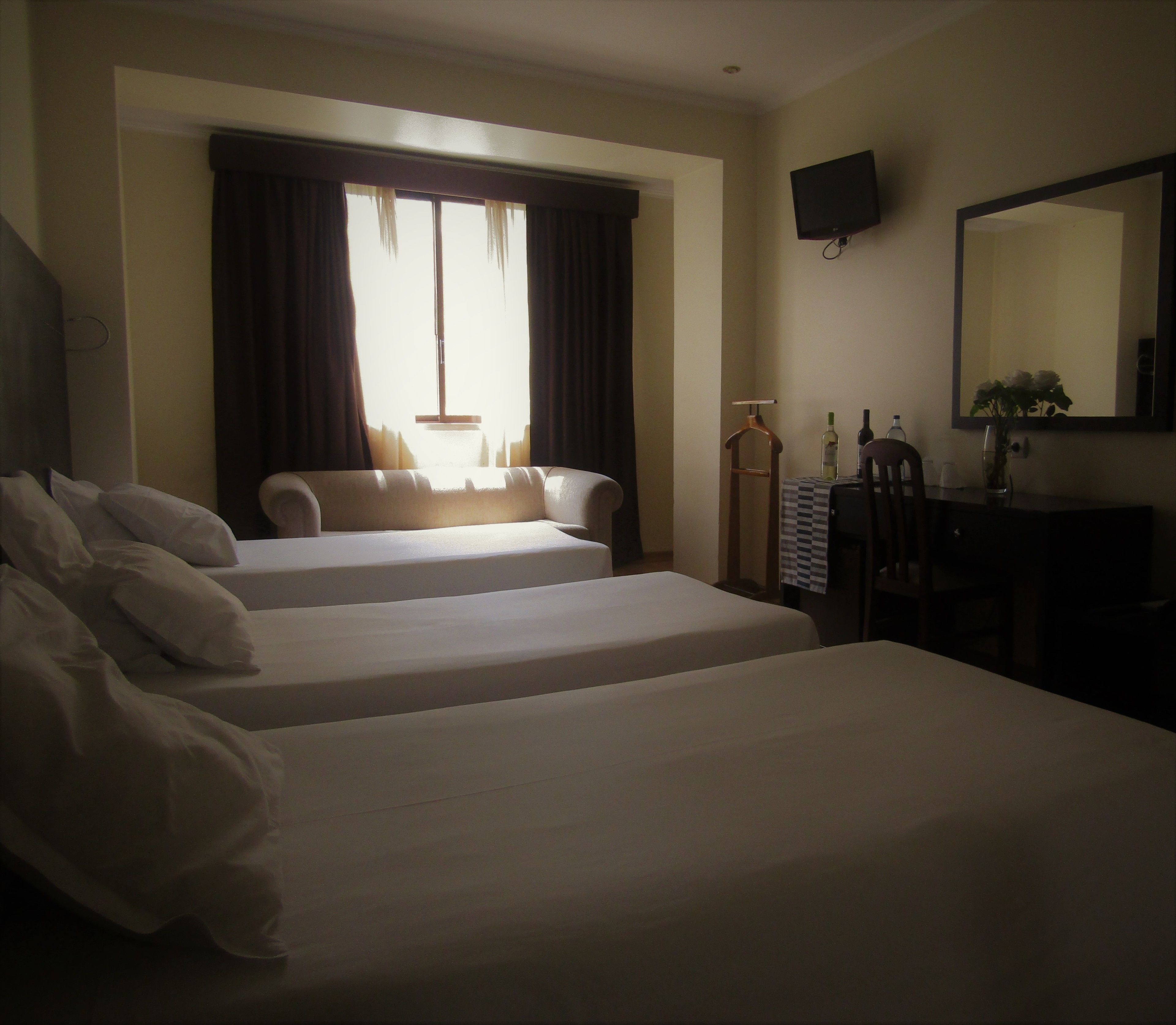 A hotel room with two beds, a desk with a chair, a mirror, and a television on the wall.