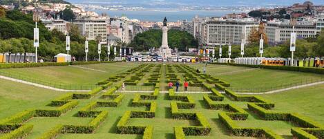 Un jardin à la française, avec un monument central, entouré de haies soigneusement taillées et offrant en arrière-plan une vue sur la ville.