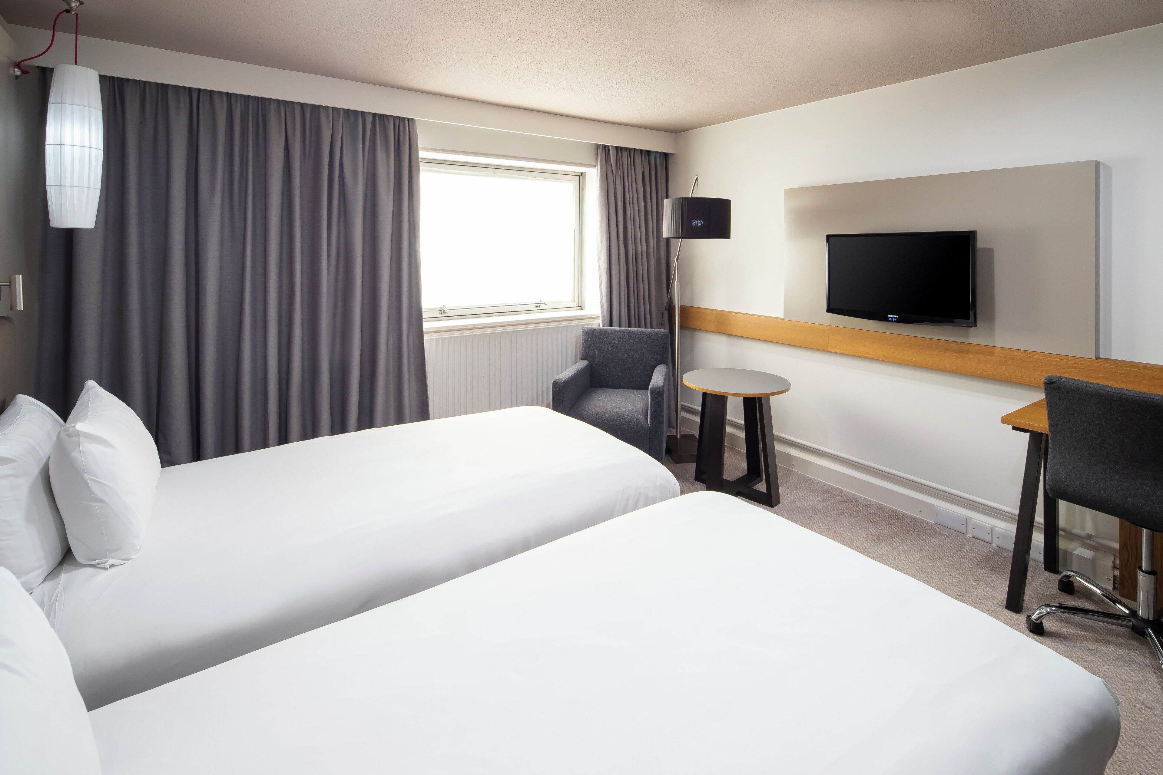 A hotel room with two beds, a TV, a small table, and a chair.