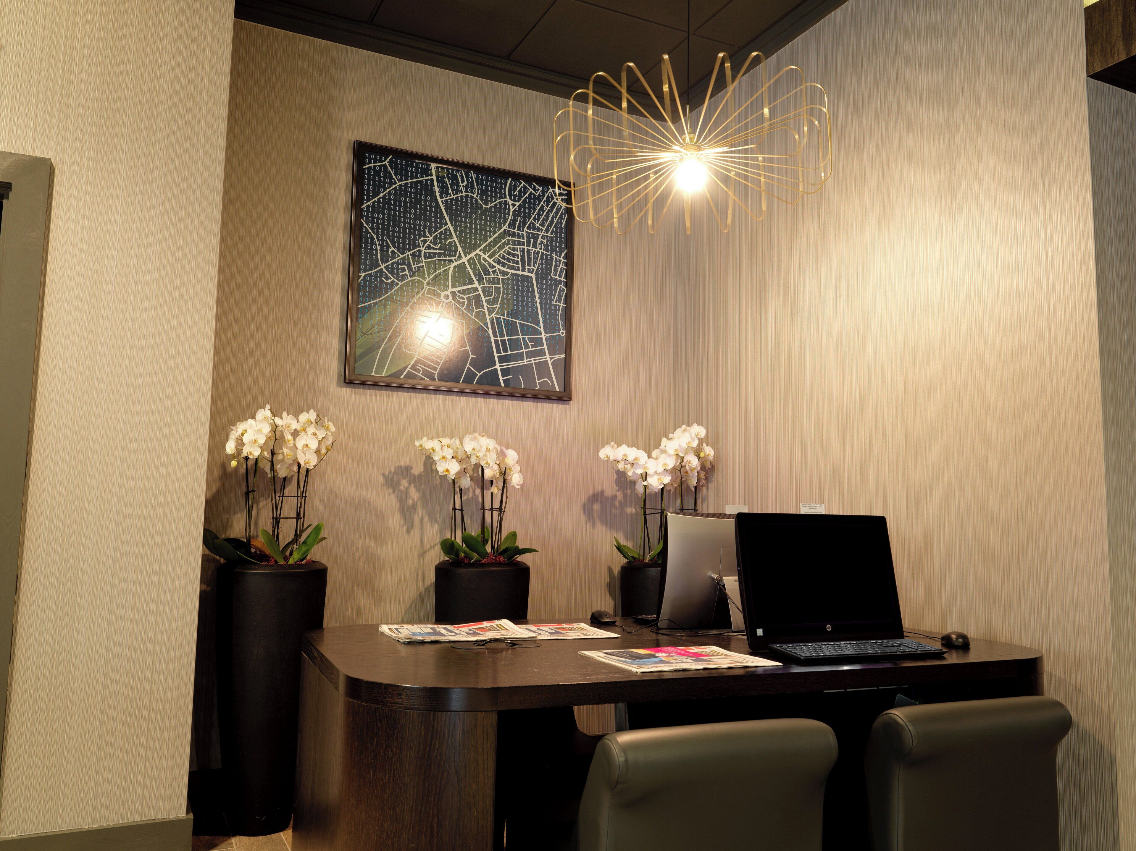 A modern office space with a desk, two chairs, a laptop, a desktop computer, and three orchid plants.