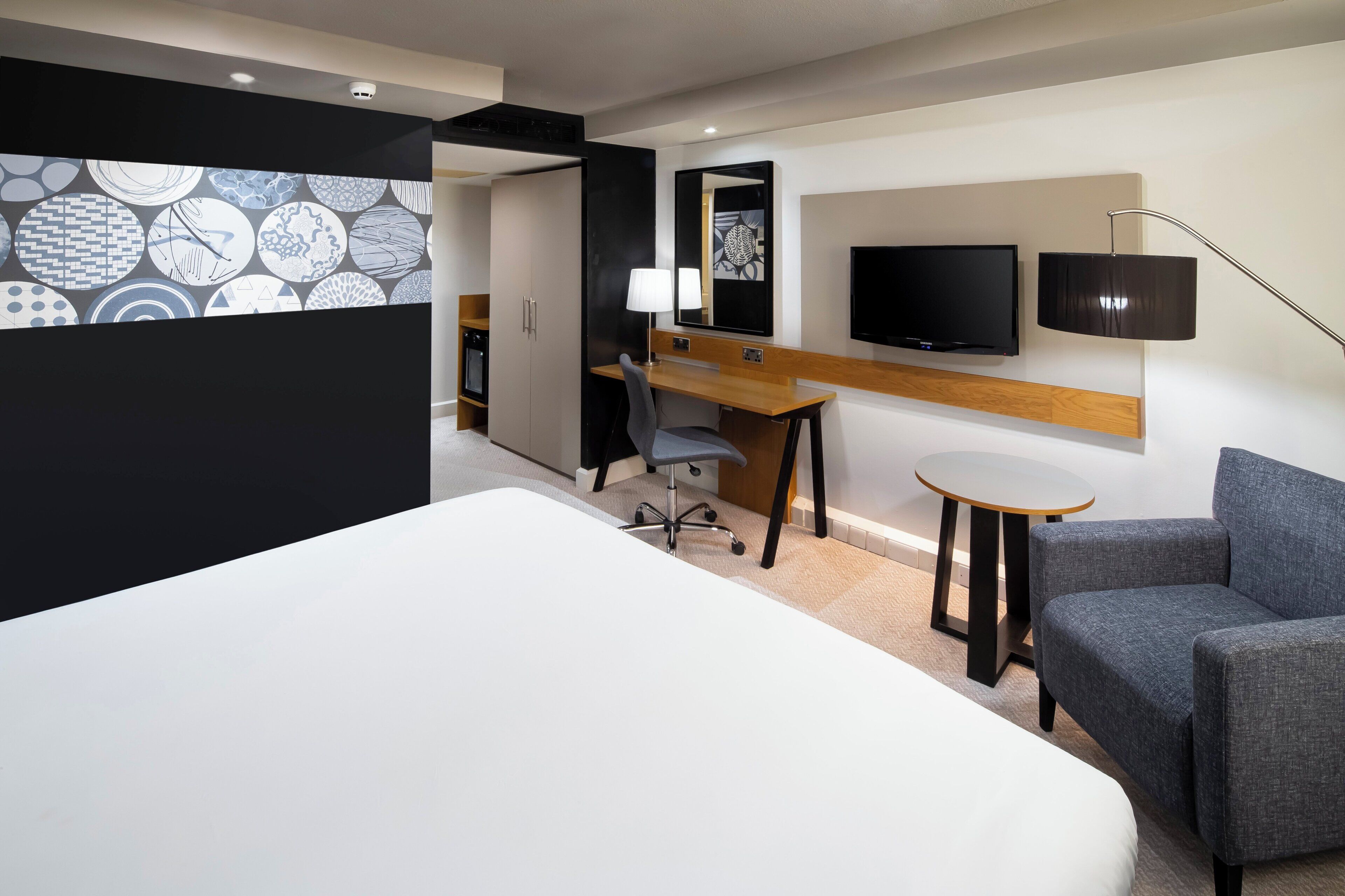 Une chambre d’hôtel avec un lit, un bureau, une chaise, une télévision et une lampe.