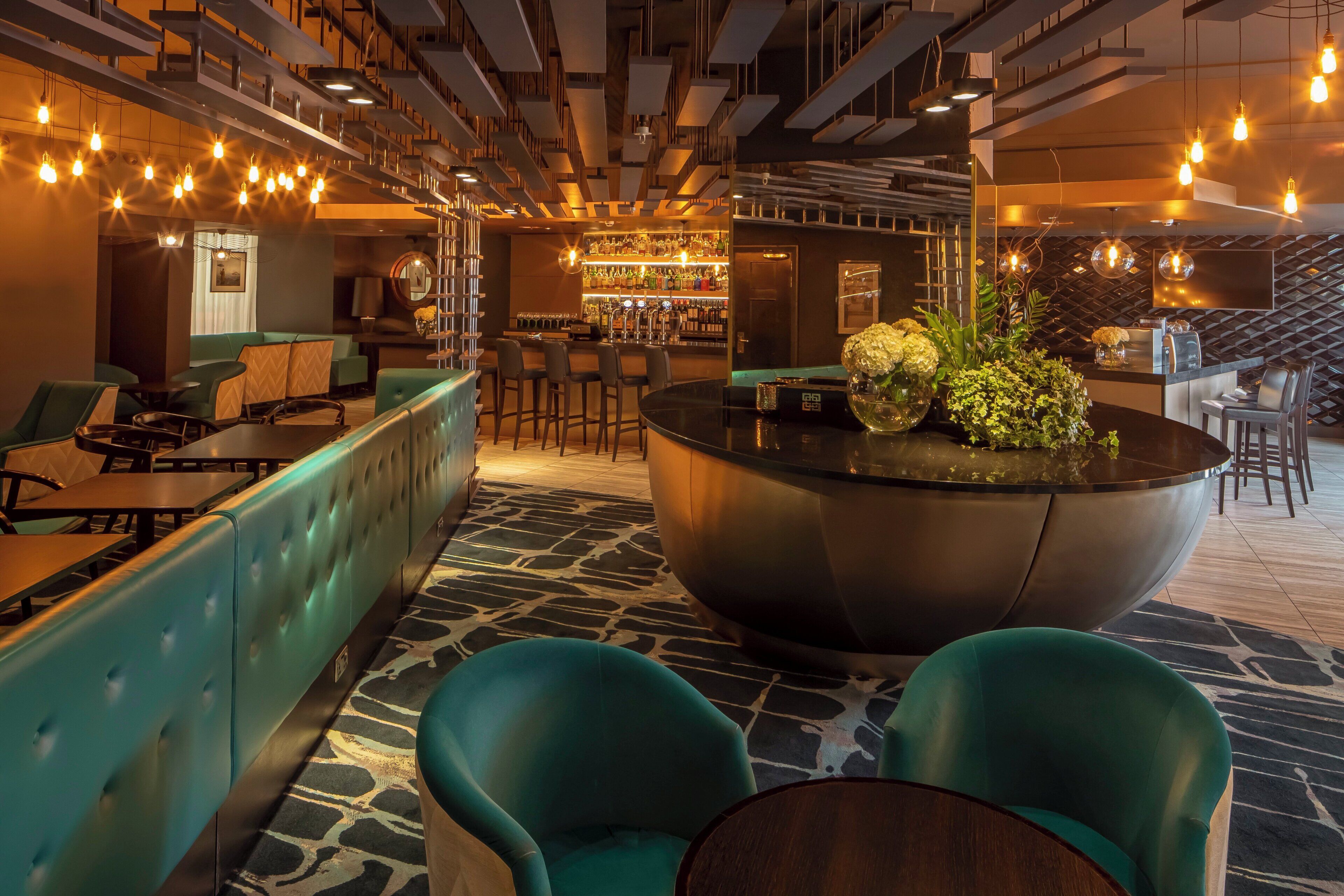 A modern bar area with seating and a bar counter, featuring a unique central seating arrangement and ambient lighting.