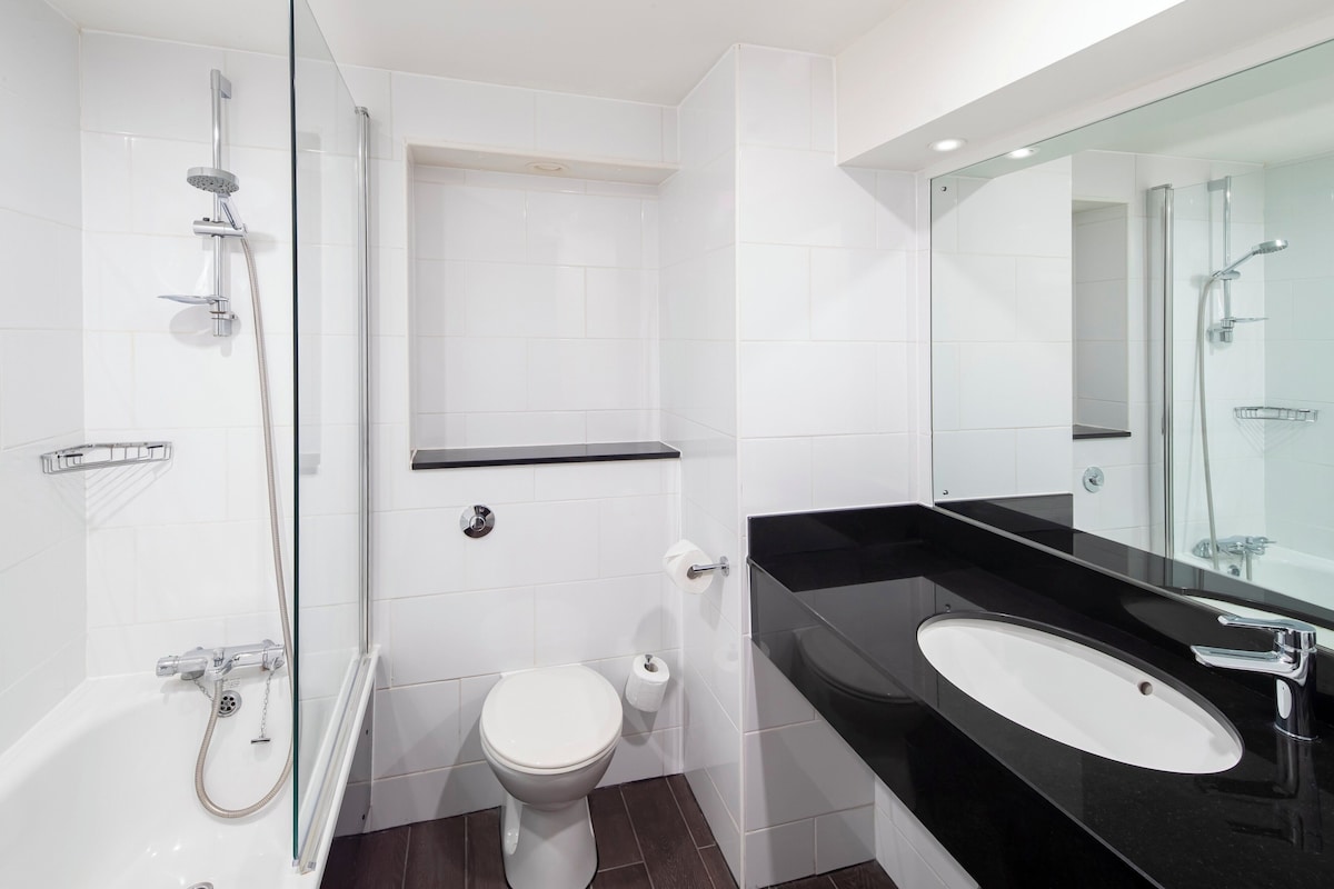 A modern bathroom with a glass shower enclosure, a white toilet, and a black sink with a large mirror.