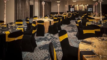 Een feestzaal met ronde tafels, zwarte stoelen met gele linten en hoge, stervormige lampen.