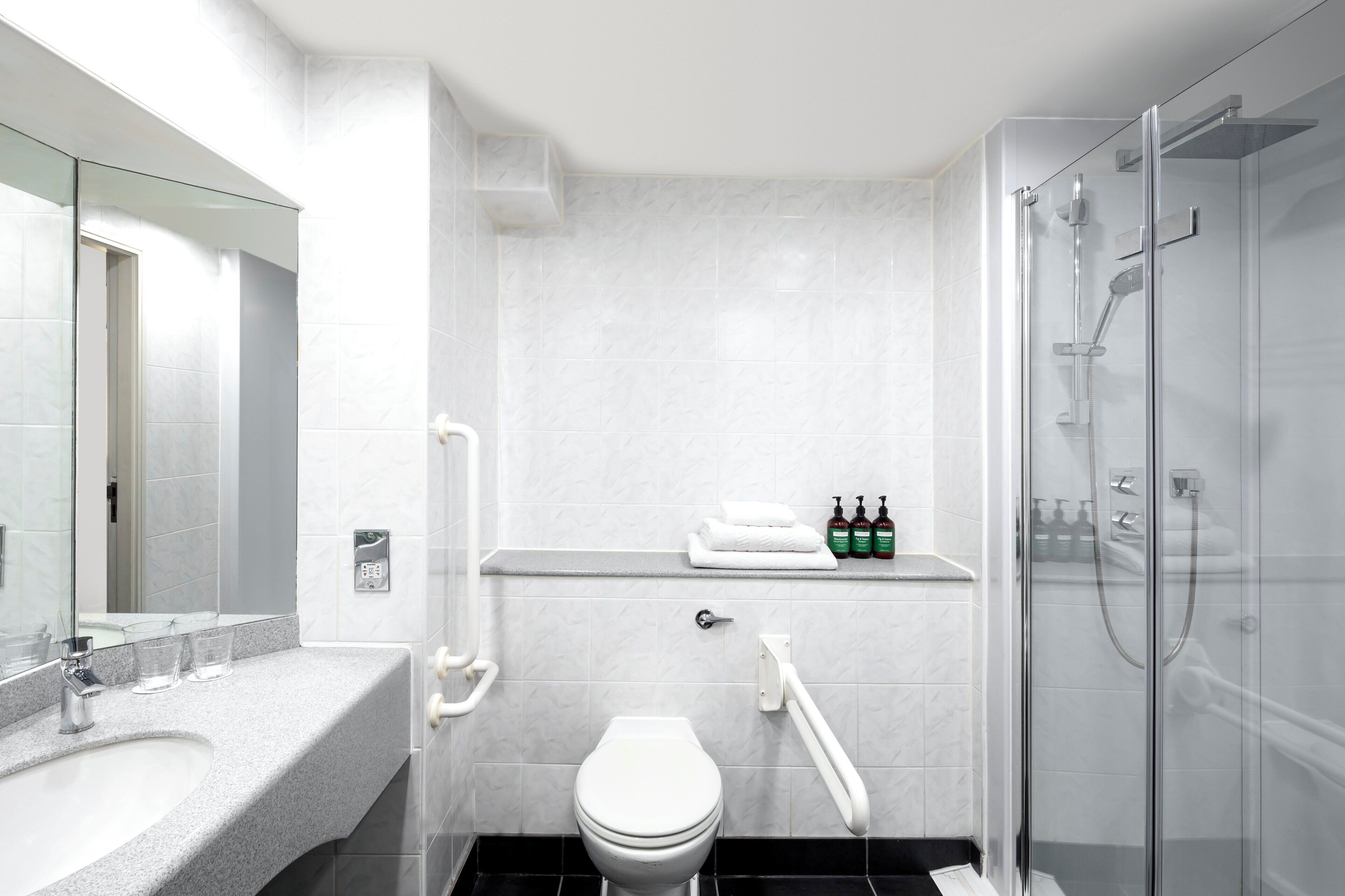 A modern bathroom with a white toilet, a glass shower enclosure, and a vanity with a mirror and sink.