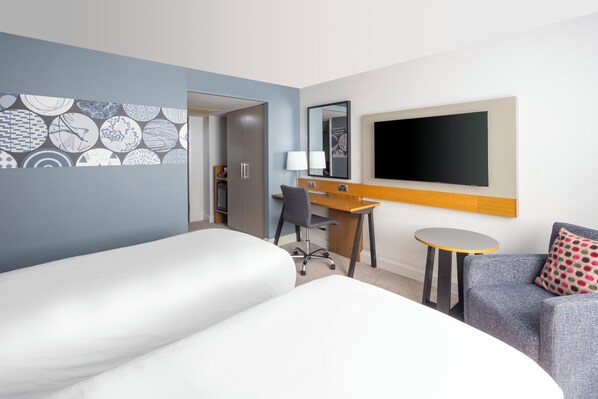 Una habitación de hotel con una cama, un escritorio, una silla, un televisor y una mesita.