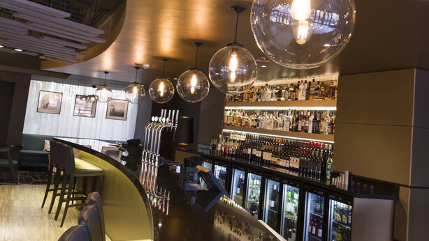 Zona de bar con varias lámparas esféricas colgantes, una barra y estantes llenos de botellas.