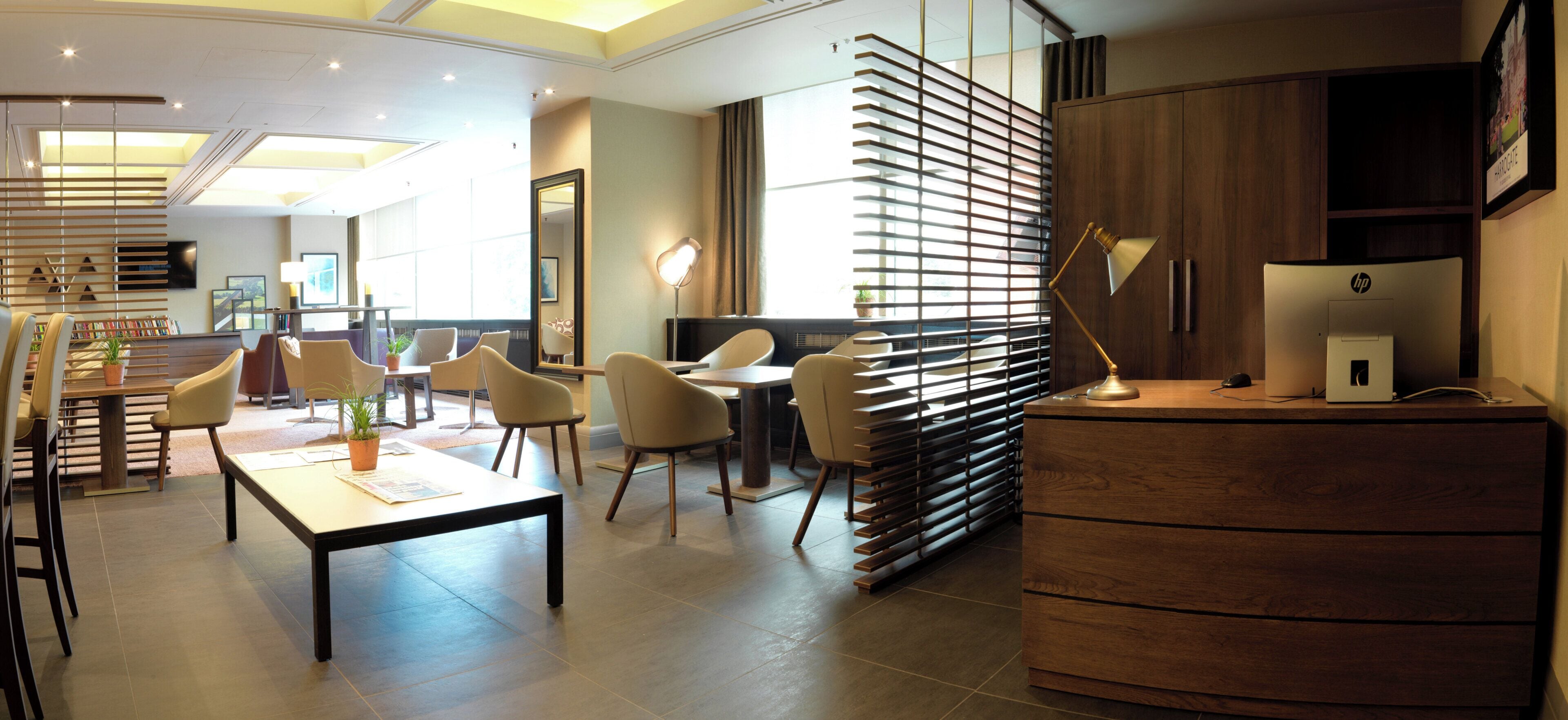 A modern hotel lobby with a reception desk, seating area, and a large window providing natural light.