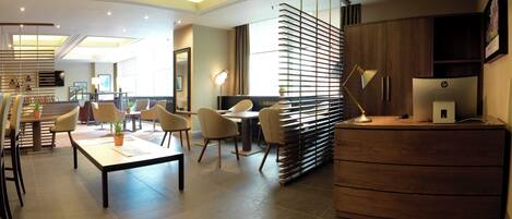 A modern hotel lobby with a reception desk, seating area, and a large window providing natural light.