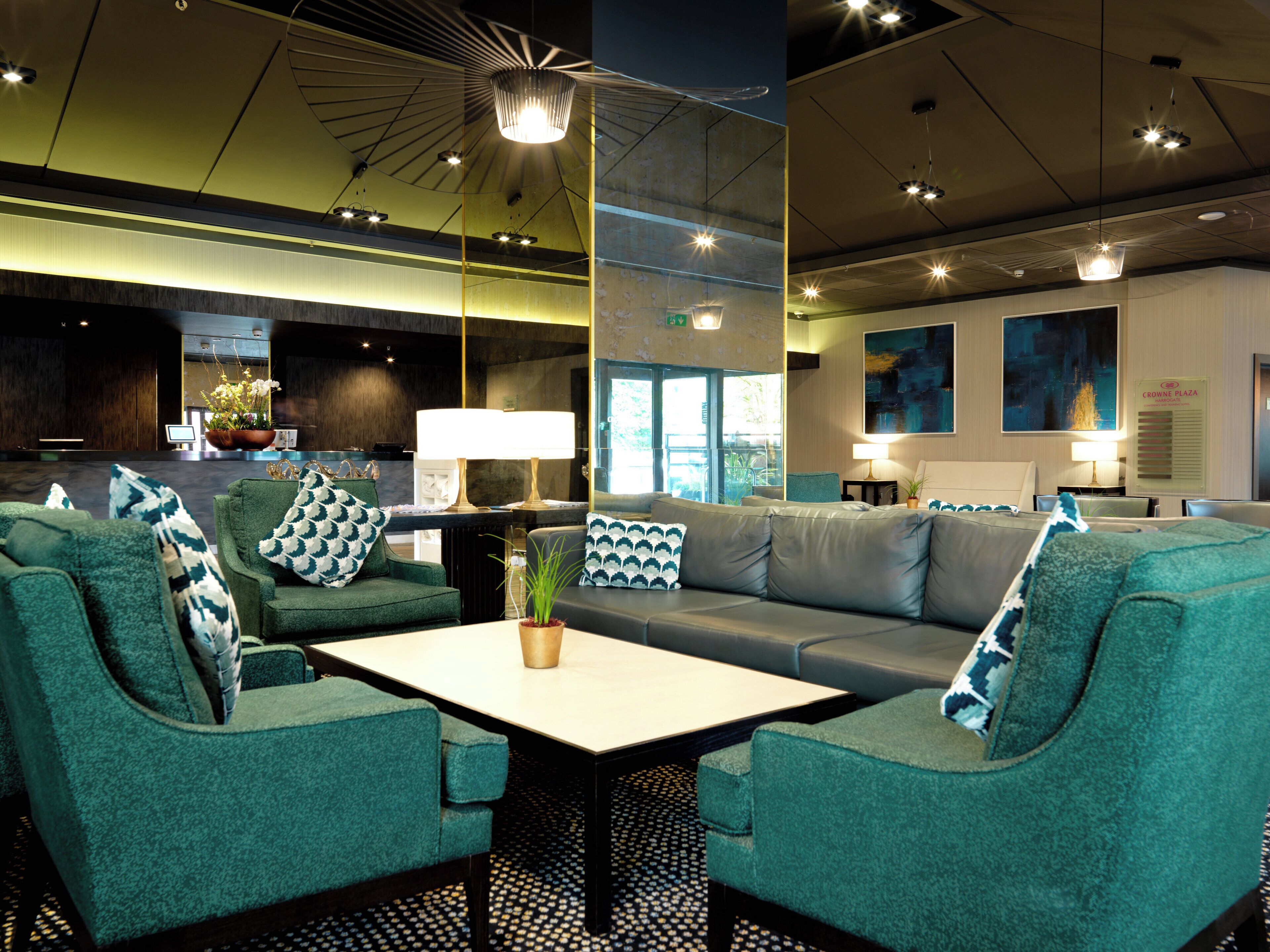 A hotel lobby with green upholstered seating, a coffee table, and a potted plant.