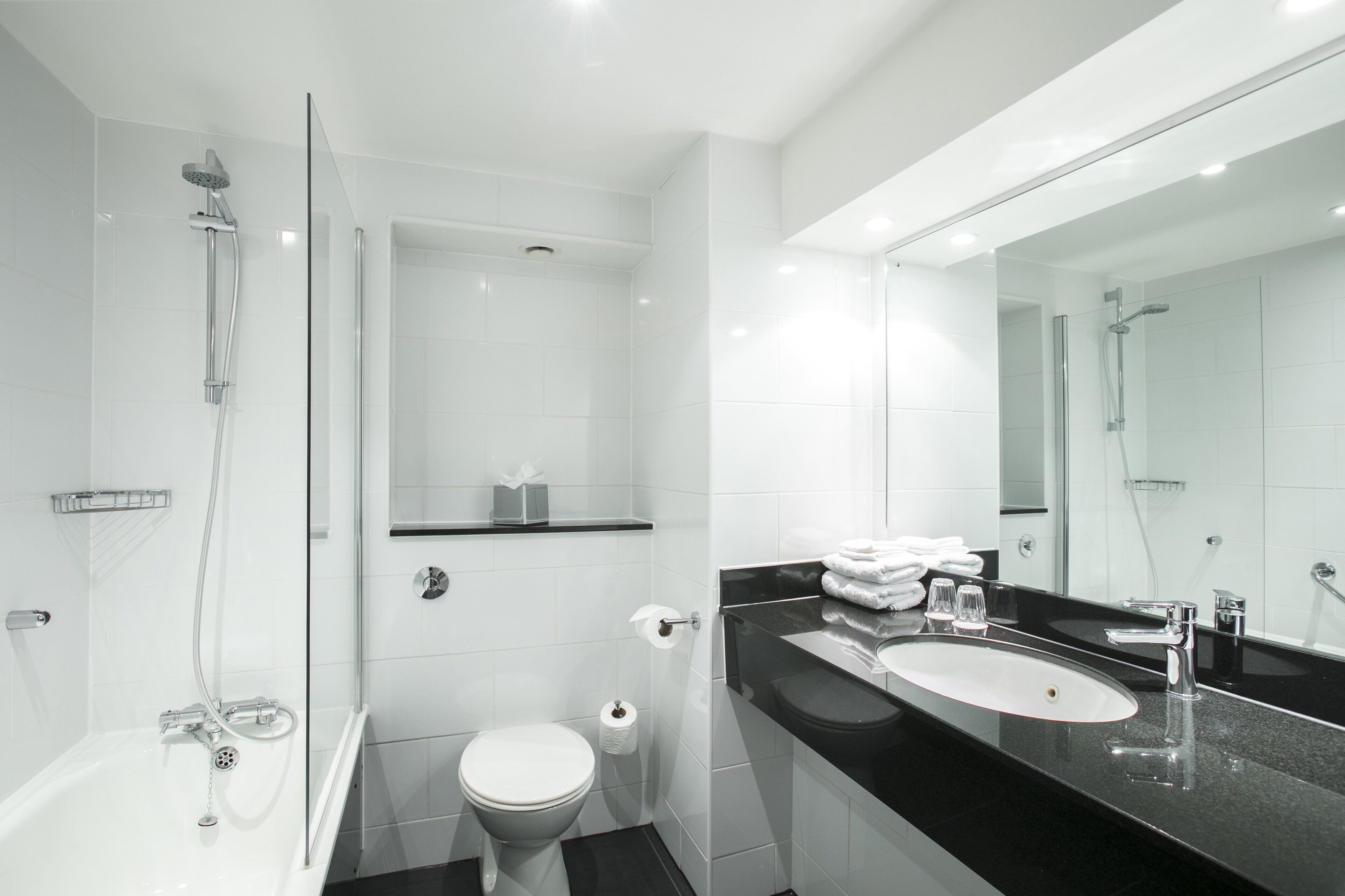 Un baño moderno con ducha envuelta en vidrio, inodoro y tocador con lavabo y espejo.