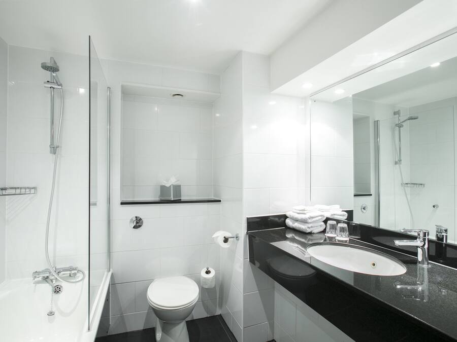 Un baño moderno con ducha envuelta en vidrio, inodoro y tocador con lavabo y espejo.
