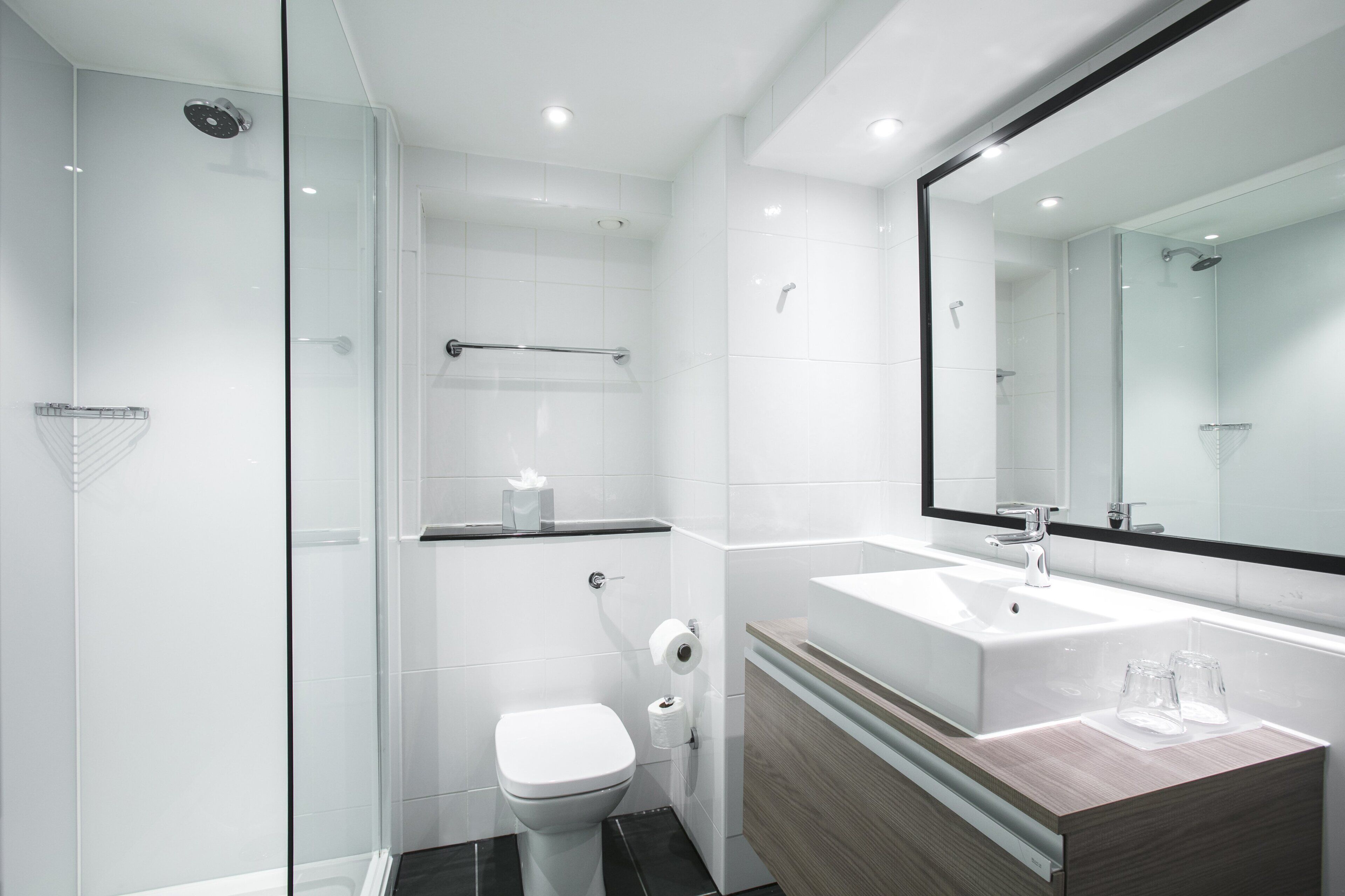 A modern bathroom with a glass shower enclosure, a white toilet, a vanity with a mirror, and a sink.