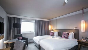 A hotel room with two beds, a desk, a chair, a TV, and a window with curtains. - Crowne Plaza Harrogate by IHG (Harrogate)