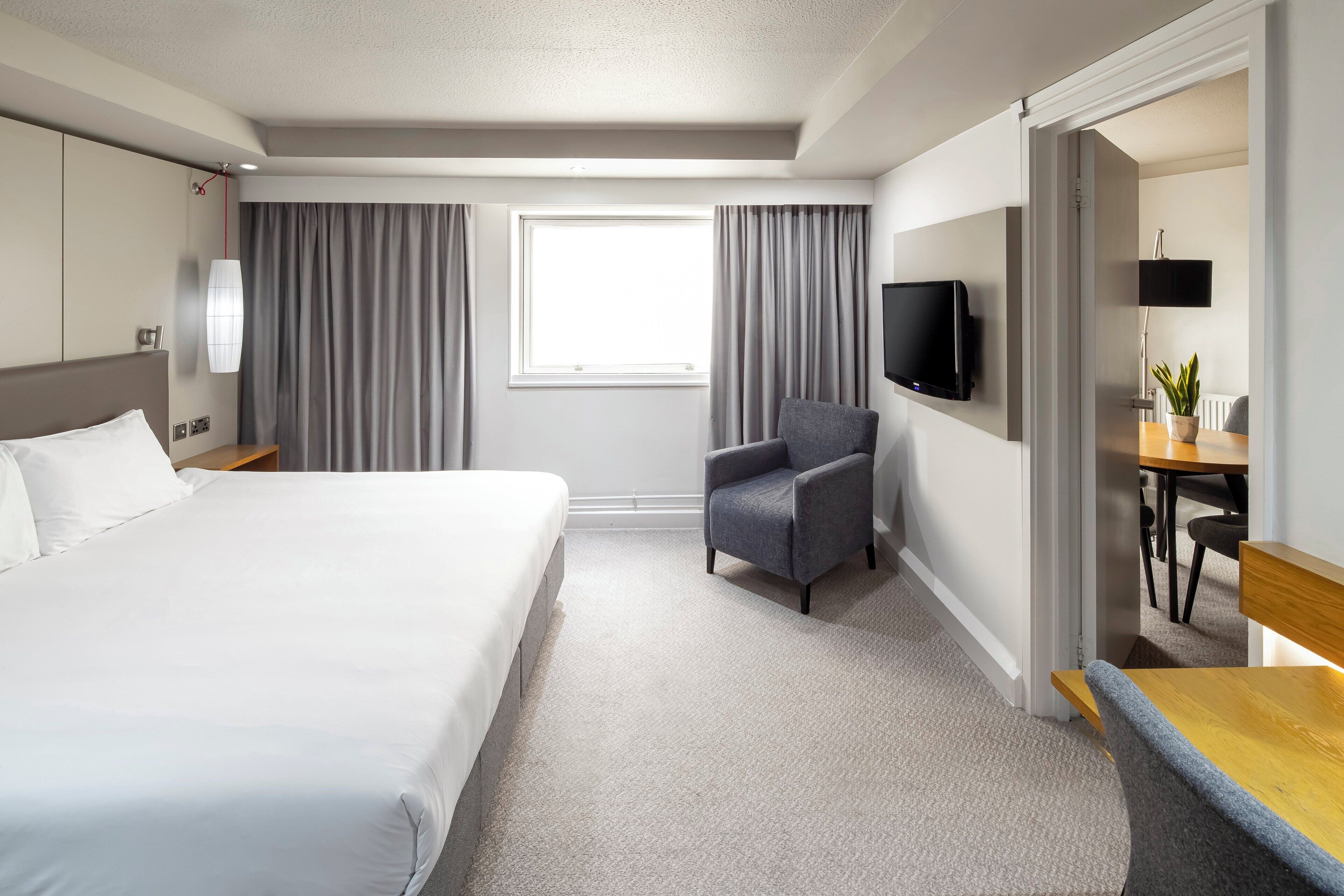 A hotel room with a large bed, a desk with a chair, a television, and a window with curtains.