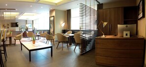 Un moderno vestíbulo de hotel con una zona de estar, un mostrador de recepción y un amplio ventanal que proporciona luz natural.
