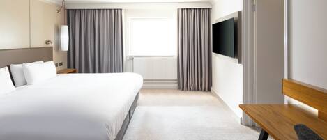 A hotel room with a large bed, a desk, a television, and a window with curtains.