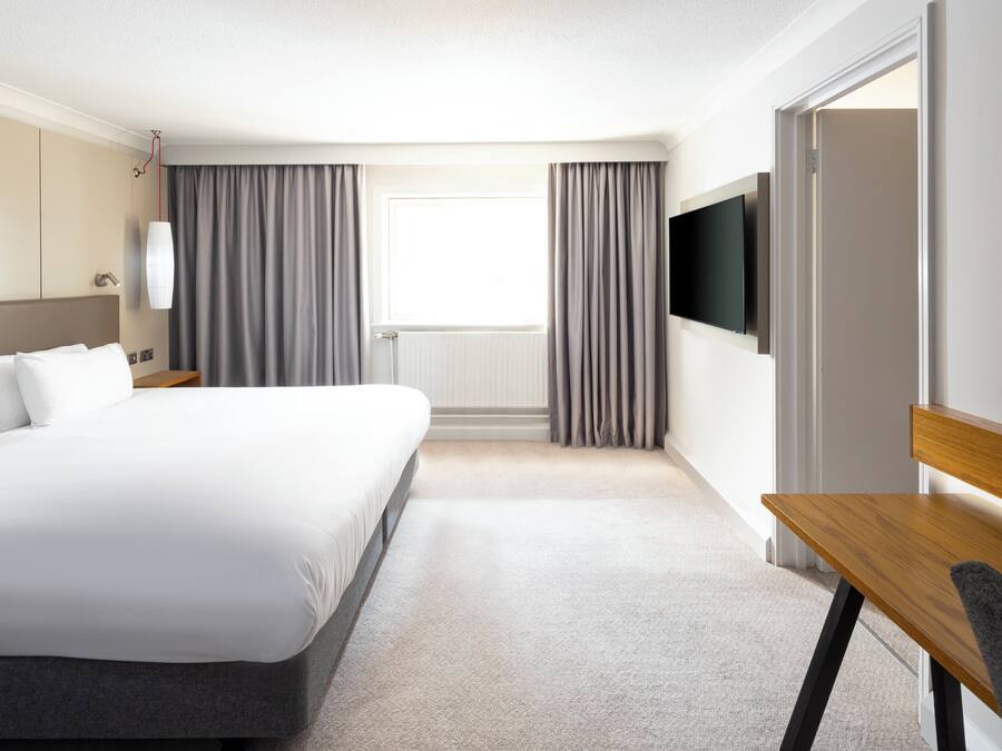 A hotel room with a large bed, a desk, a television, and a window with curtains.
