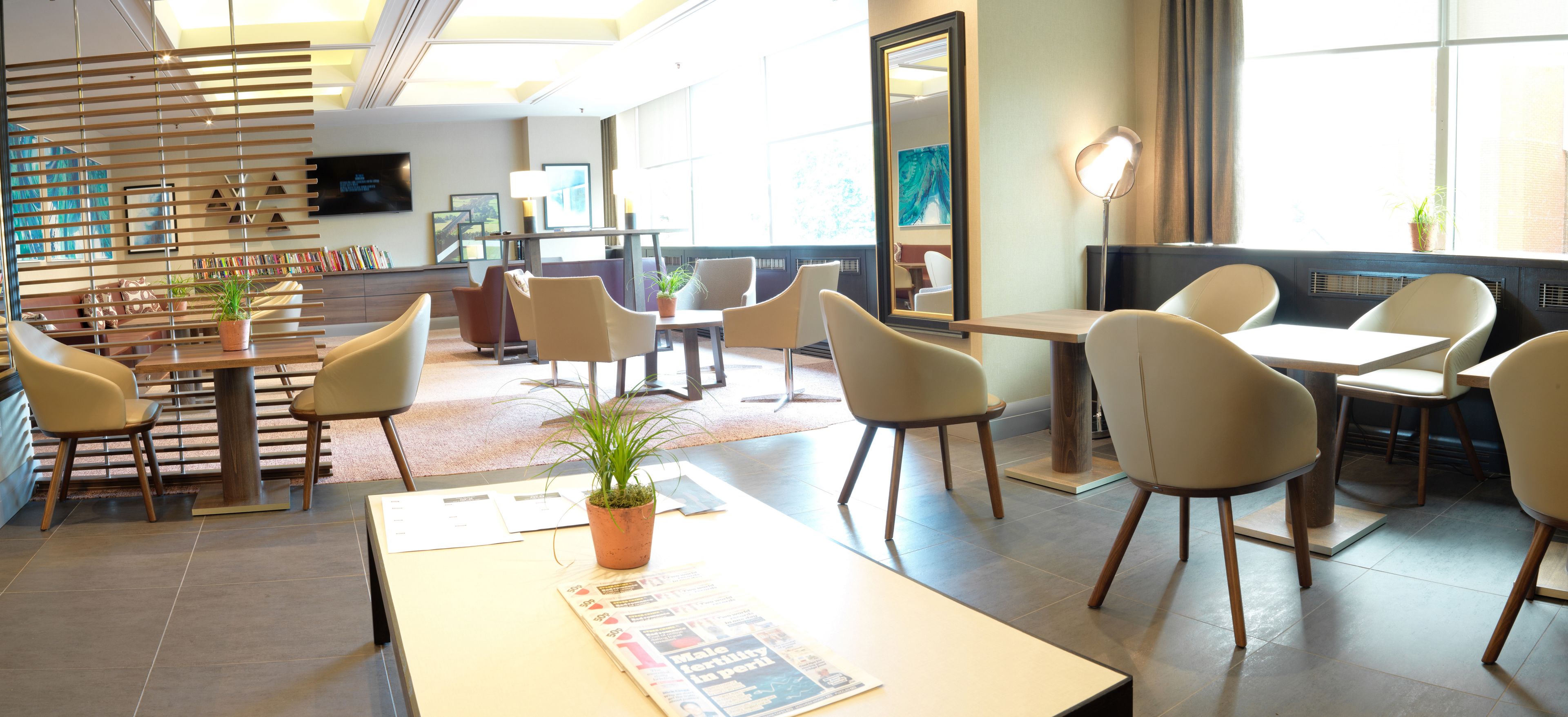 A modern hotel lobby with a mix of seating options, including tables and chairs, and a large window providing natural light.