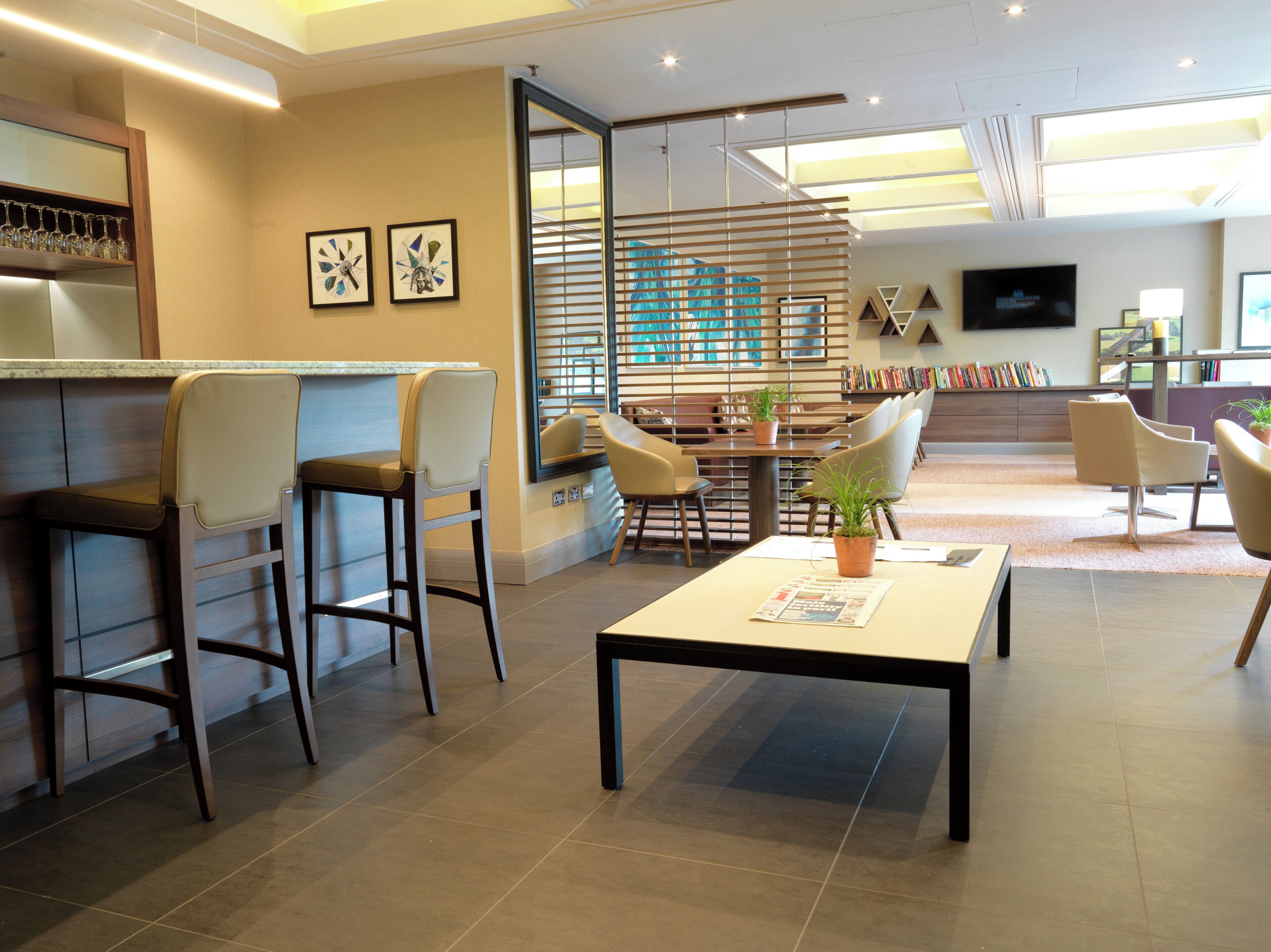 A modern hotel lobby with a bar area, seating, a television, and a large window.