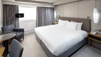 Una habitación de hotel con una cama grande, un escritorio, una silla, un televisor y una ventana con cortinas.