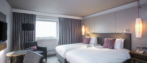 Habitación de hotel con cama, mesitas de noche, escritorio, silla, televisión y ventana con cortinas.