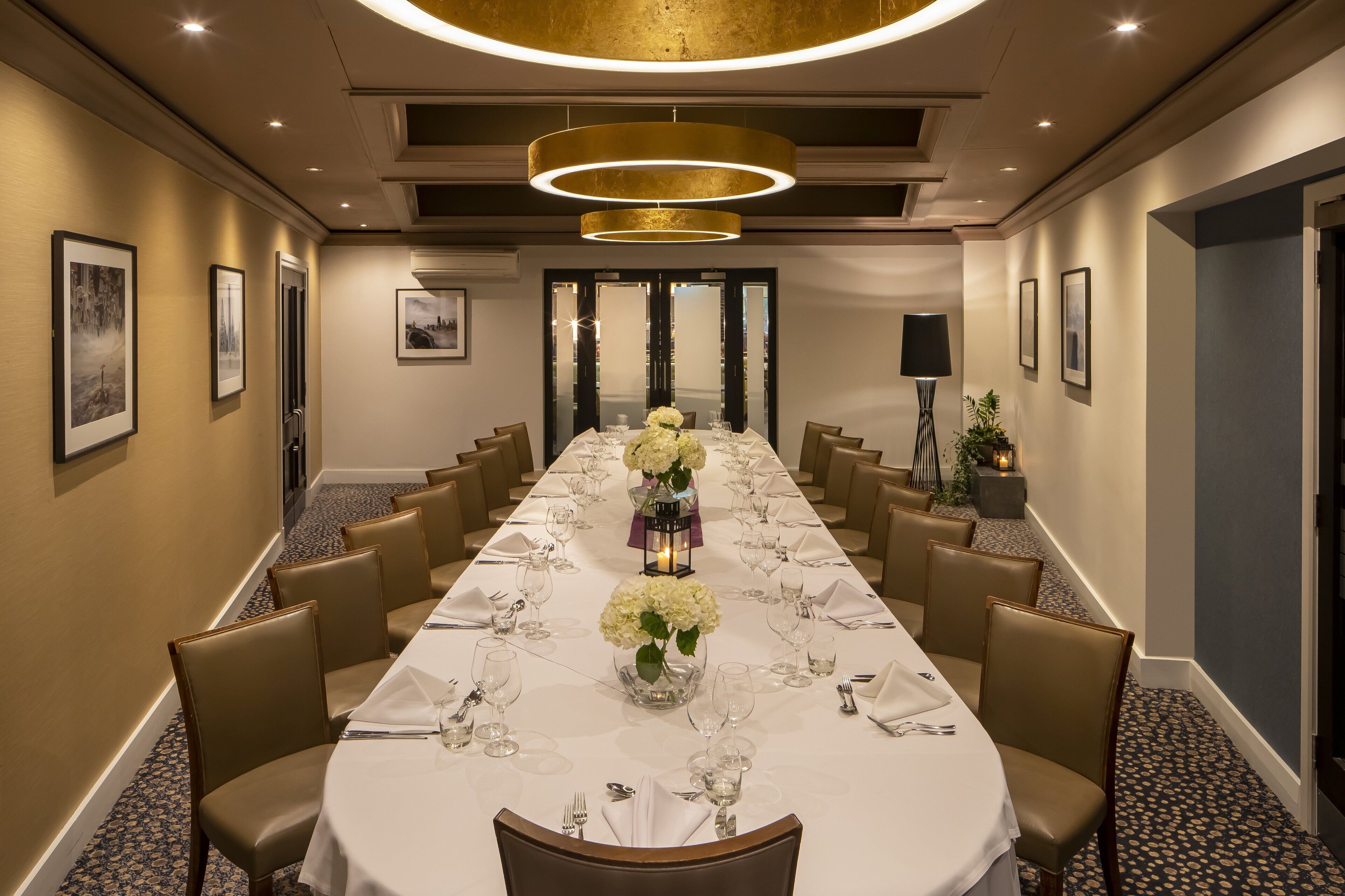 A long conference table set for a meeting with chairs on both sides, framed pictures on the walls, and a modern chandelier.