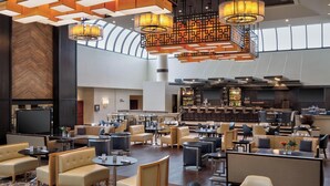 A spacious hotel lobby with multiple seating areas, a bar, and a large screen. - Sheraton DFW Airport Hotel (Irving)