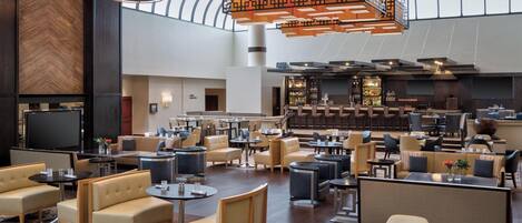 A spacious hotel lobby with multiple seating areas, a bar, and a large screen.