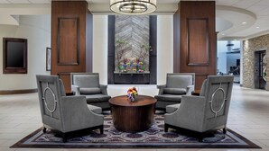 A lobby with a round wooden coffee table, four grey armchairs, a large chandelier, and a decorative wall with a chevron pattern. - Sheraton DFW Airport Hotel (Irving)