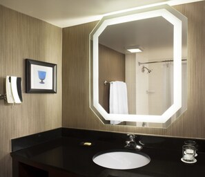 A modern bathroom with a large mirror, a black countertop, a white sink, and a framed picture on the wall. - Sheraton DFW Airport Hotel (Irving)