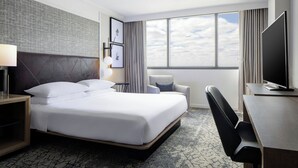 A hotel room with a large bed, a desk, a chair, and a TV. - Sheraton DFW Airport Hotel (Irving)