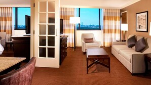 A hotel room with a city view, a sofa, a chair, a desk, and a television. - Sheraton DFW Airport Hotel (Irving)