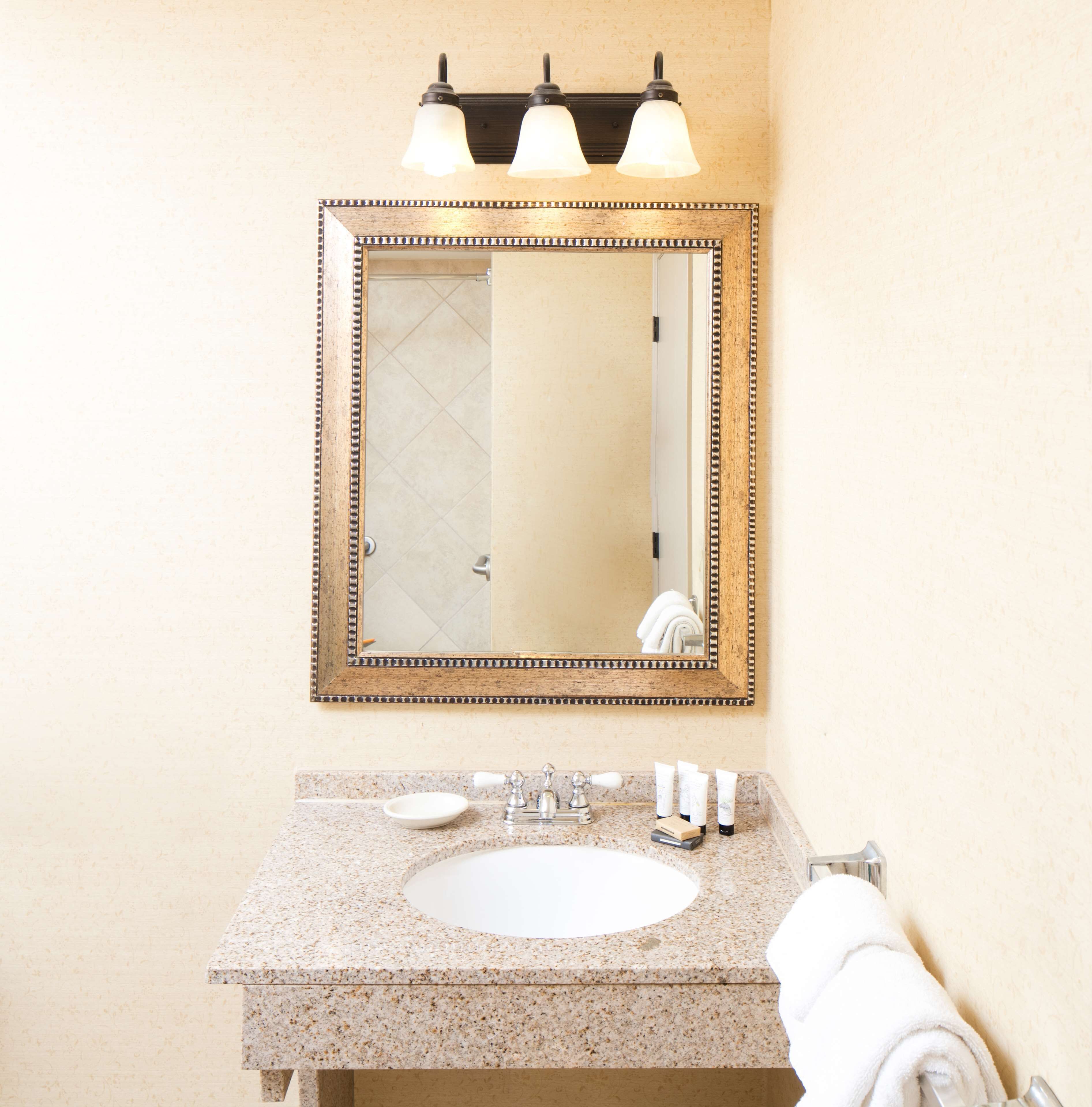 Une salle de bain avec un lavabo doté d’un plan de travail en granit, un miroir avec un cadre décoratif et un porte-serviettes.