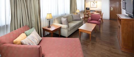 A modern hotel room with a living area featuring a sofa, armchairs, a coffee table, and a TV.