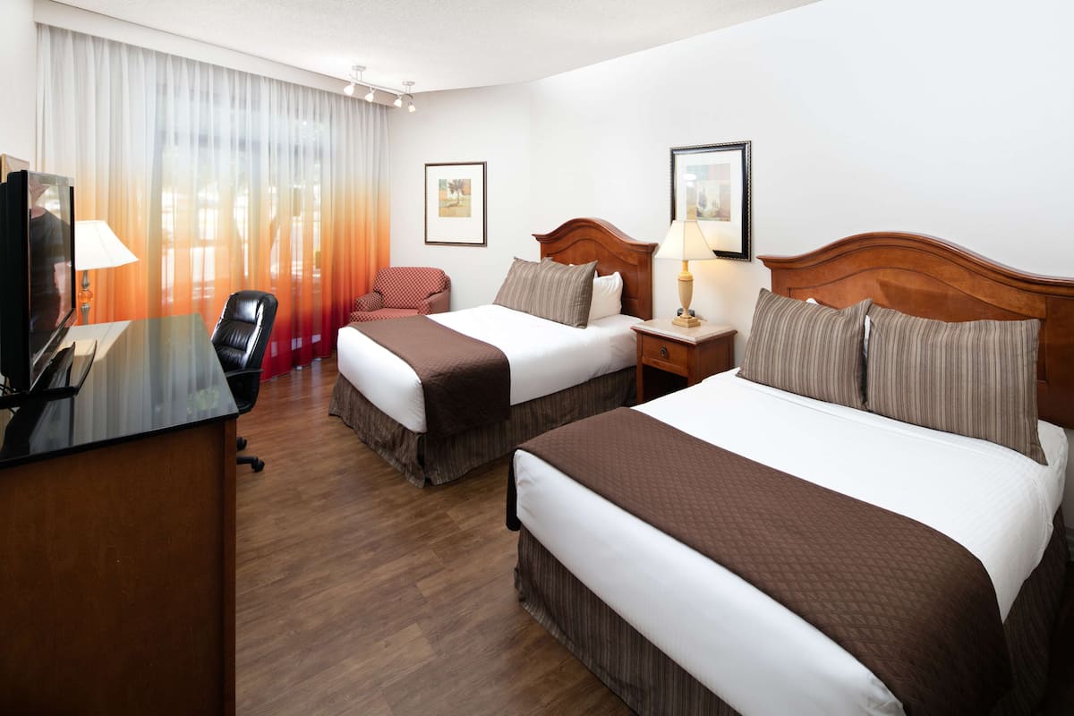 A hotel room with two beds, a desk, a TV, and a chair.