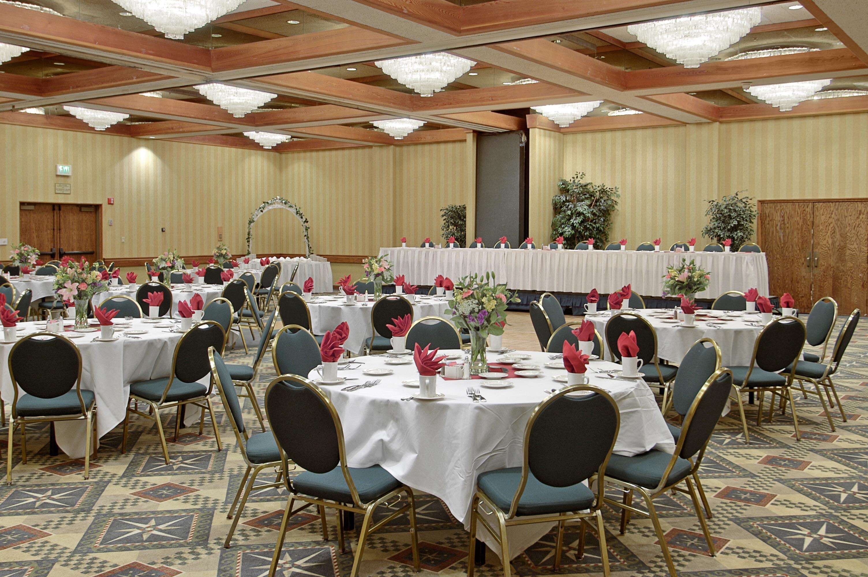 Une salle de banquet avec des tables rondes dressées pour un événement formel, agrémentée de nappes blanches, de chaises dorées et de compositions florales en guise de centre de table.