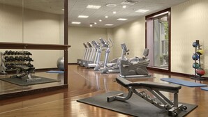 A gym with exercise equipment, a mirror, and a window with blinds.