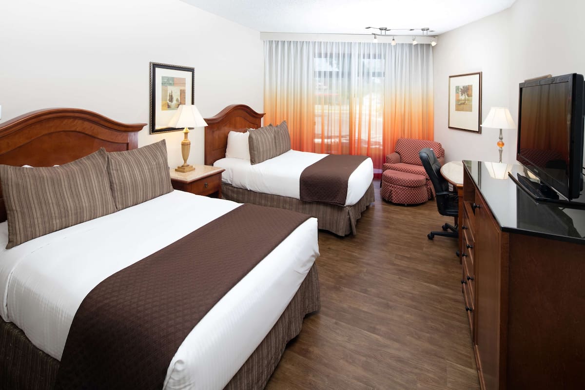A hotel room with two beds, a TV, a desk, and a chair.