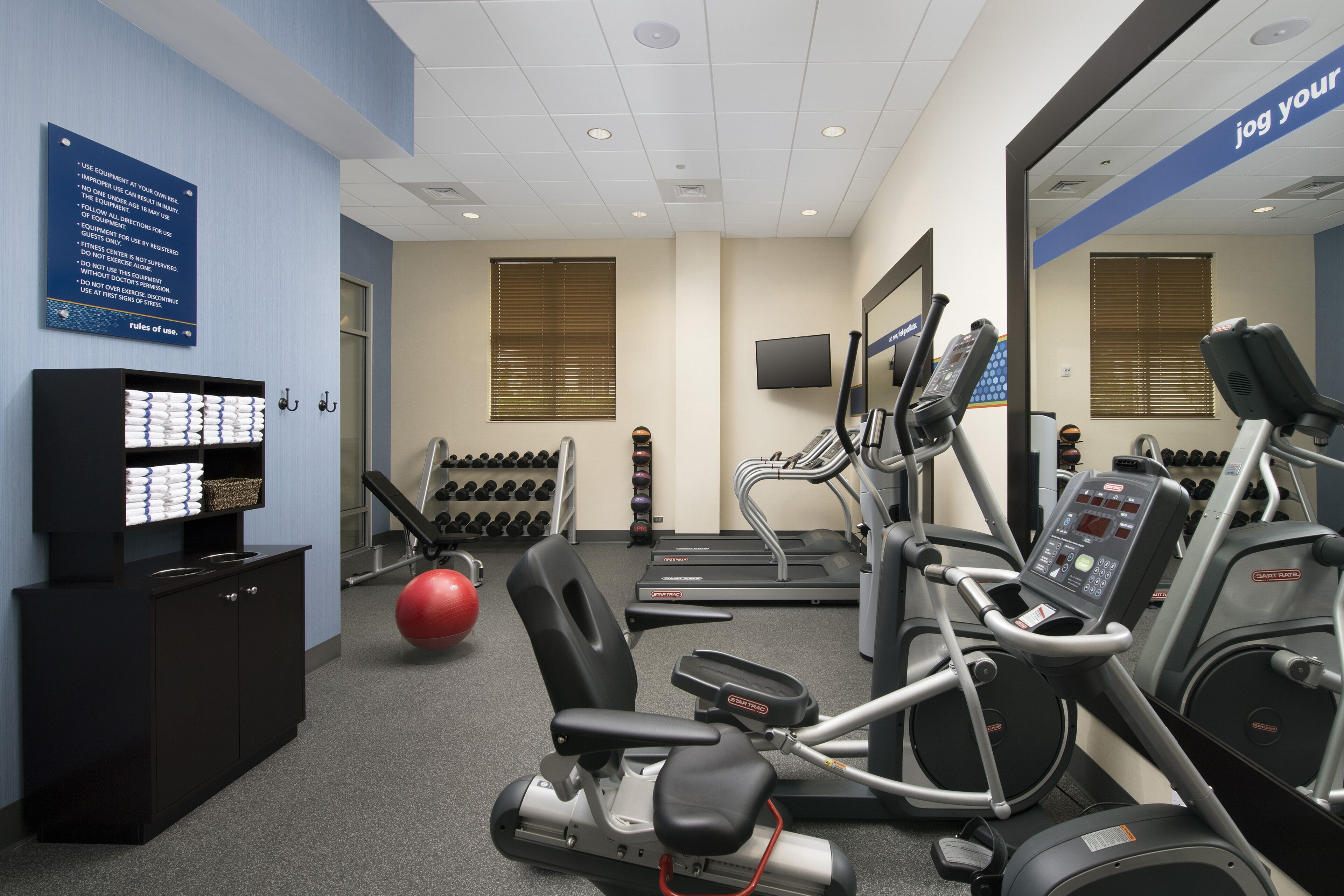 A gym with treadmills, elliptical machines, and a red exercise ball.
