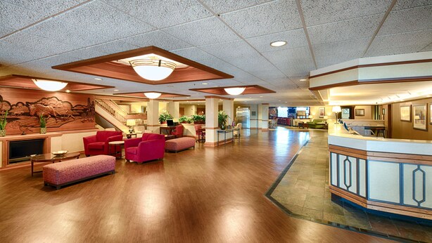 A spacious lobby with a wooden floor, red seating, a reception desk, and a staircase leading to upper floors.