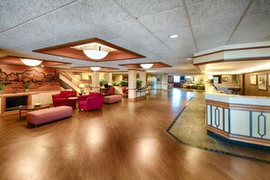 Un vestíbulo amplio con piso de madera, asientos rojos, un mostrador de recepción y una escalera que lleva a pisos superiores.