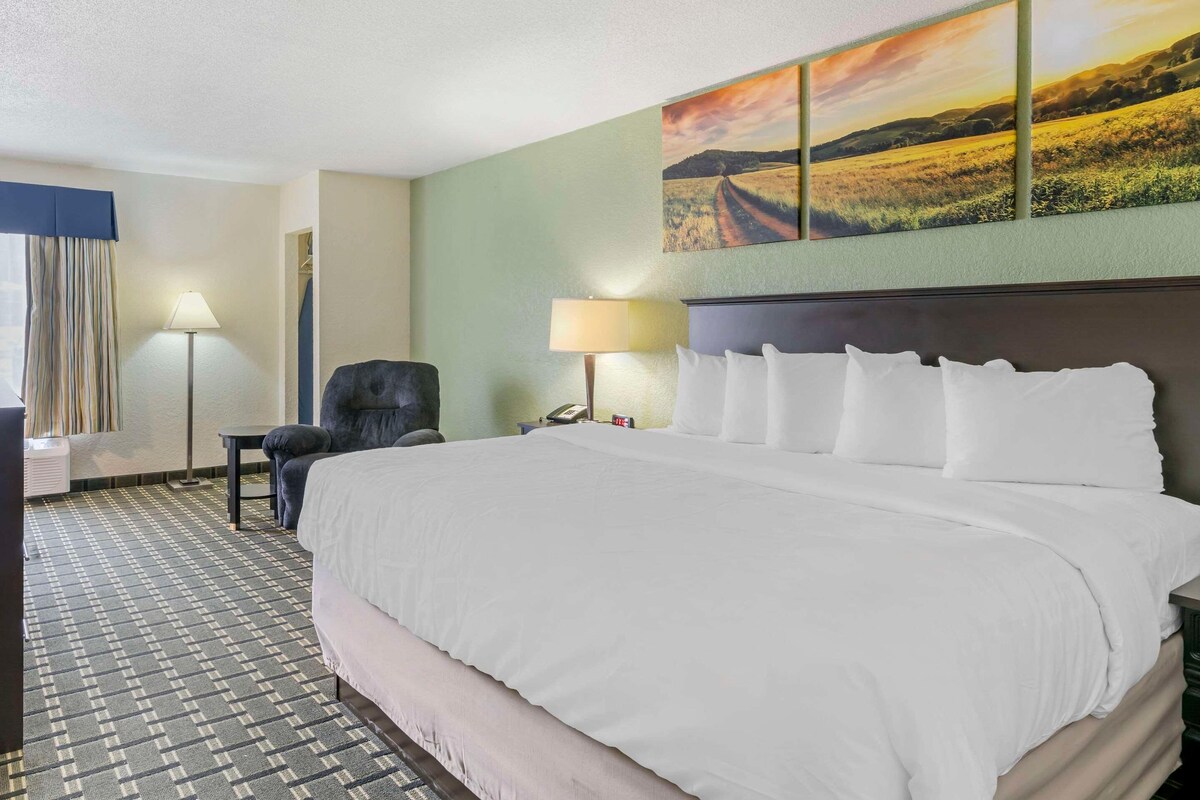 A hotel room with a large bed, two bedside lamps, a chair, a desk, and a painting on the wall.