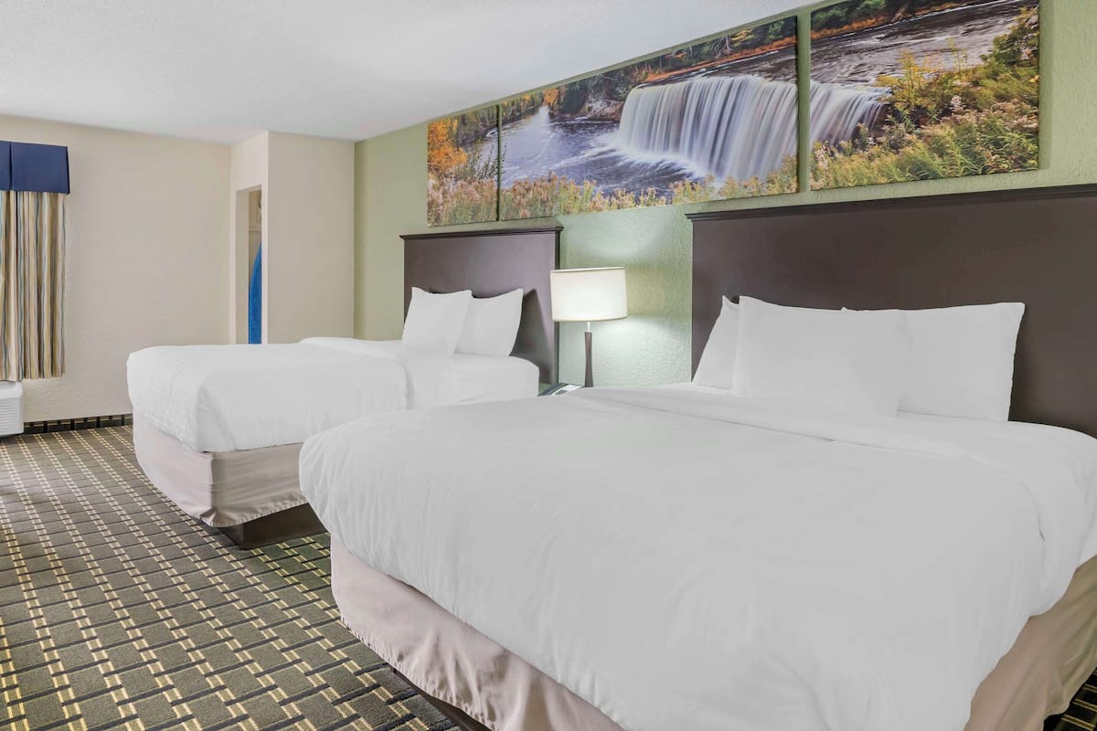 A hotel room with two beds, a large painting of a waterfall, and a patterned carpet.