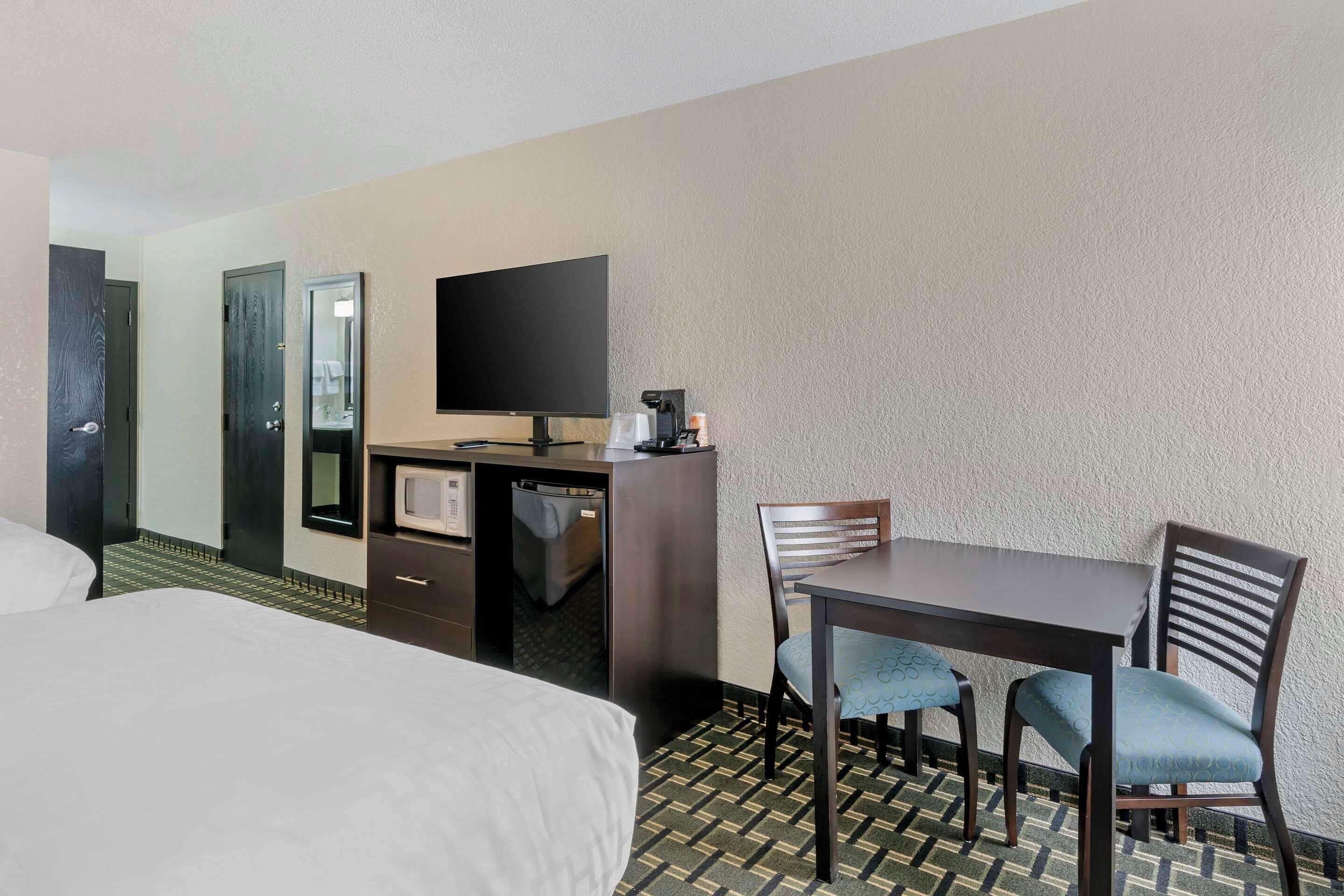 Una habitación de hotel con una cama, un escritorio con computadora, un televisor y una silla.