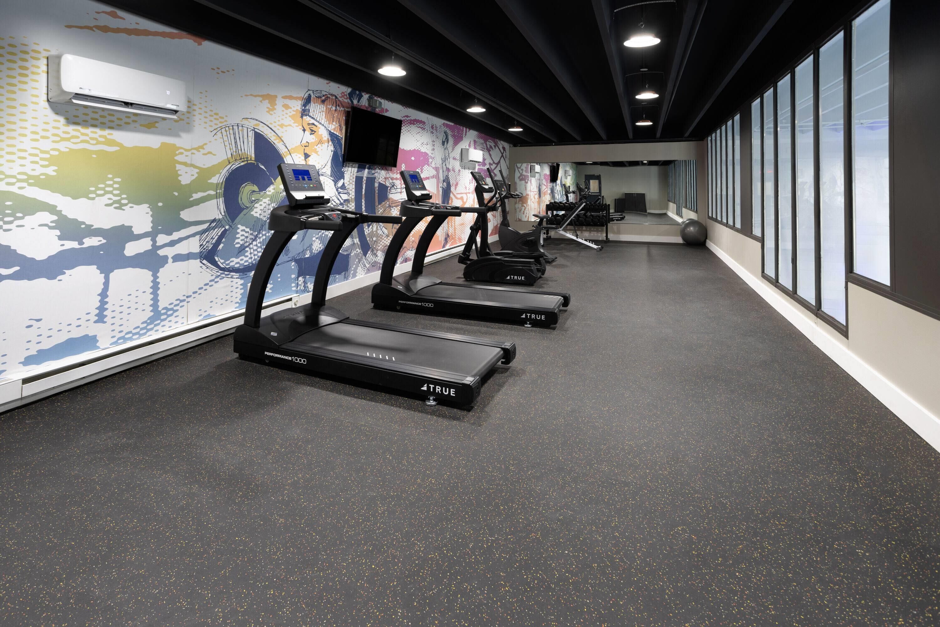A gym with treadmills, a wall-mounted TV, and a large window.