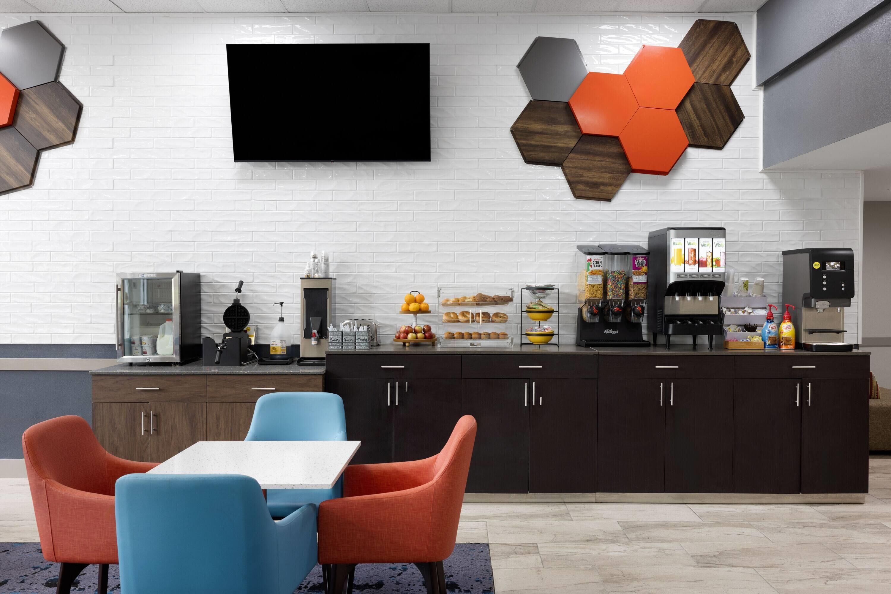 A modern kitchen with a flat-screen TV, hexagonal wall decor, and a coffee station.